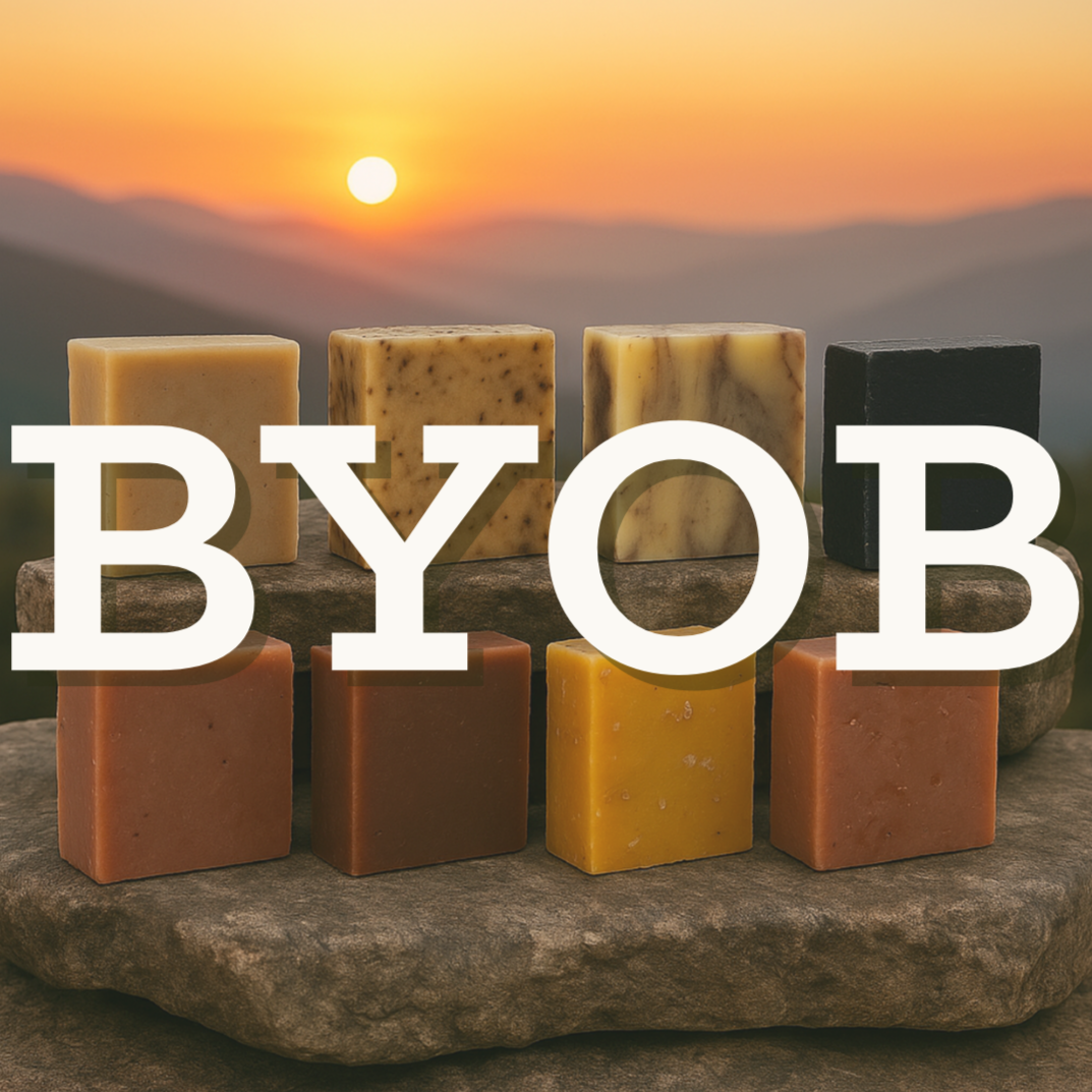 Assorted bars of soap on a rock with a sunset background and 'BYOB' text.